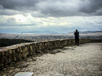 a man in black is standing on the platform of the acroplis in athens to take a picture of the metropolis