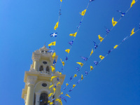 in front of the nice blue sky ist the church tower of ialysos on rhodes with greek flags and flags of the greek orthodox