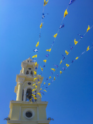in front of the nice blue sky ist the church tower of ialysos on rhodes with greek flags and flags of the greek orthodox