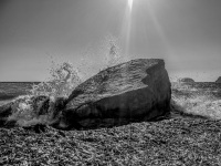 a wave hits a big rock at the fourni beach on rhodes at backlit, black-and-white