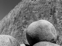 three big cannonballs are standing at the wall of the grandmaster palace in the old town of rhodes, black-and-white