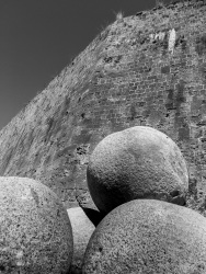 three big cannonballs are standing at the wall of the grandmaster palace in the old town of rhodes, black-and-white