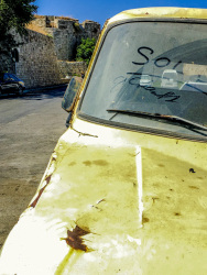a yellow oldtimer is standing in rhodes city, in the background is the wall of the grandmaster palace