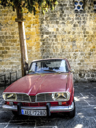 in front of a yello wall in the old town of rhodes is a red renault 16