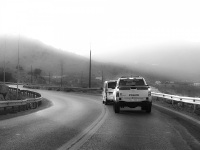 the left turn of a street near lindos on rhodes with a car and behind a police car, black-and-white