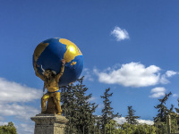 a golden coloured street artist ist holding a big world on his shoulders in thiseio in athens