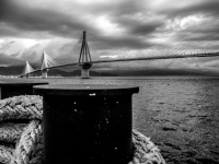 behind a big black harbor pollard and thick ropes you see the rio-andirrio-bridge in patras, black-and-white