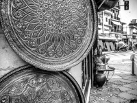 two big pewter plates are hanging outside a shop at the street in ioannina leading to molos, black-and-white