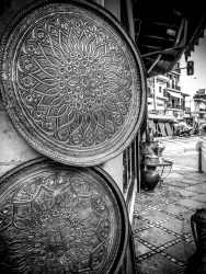 two big pewter plates are hanging outside a shop at the street in ioannina leading to molos, black-and-white