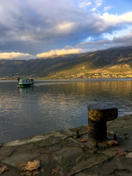 behind a rosty harbor bollard is the lake pamvotida in ioannina with a boat in a nice evening light
