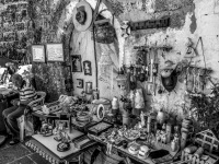 an old man is sitting inside of his collection of flea market things in the old town of rhodes, black-and-white