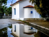 a little white chapel in diakopto reflects in a big puddle in front of it