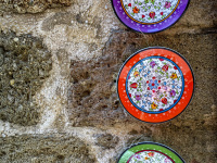 three colorful homemade ceramic plates are hanging on a beige stonewall in the old town of rhodes