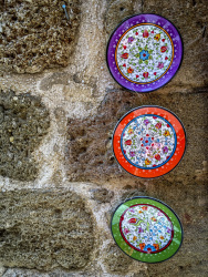 three colorful homemade ceramic plates are hanging on a beige stonewall in the old town of rhodes