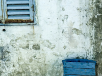 an old grey wall with peeling plaster, with a blue window and a blue greek chair in agios isidoros on rhodes