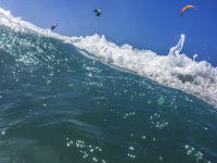 a wave with sea foam in the front and kitesurfer at the blue sky behind the szene in prasonisi on rhodes