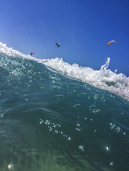 a wave with sea foam in the front and kitesurfer at the blue sky behind the szene in prasonisi on rhodes