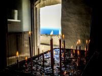in the chapel in monolithos on rhodes burning candles are in the front with a view out of the door to the sea