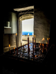 in the chapel in monolithos on rhodes burning candles are in the front with a view out of the door to the sea