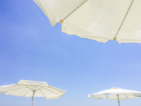 three white beach umbrellas are in front of a light blue sky in charaki on rhodes