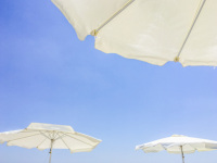 three white beach umbrellas are in front of a light blue sky in charaki on rhodes