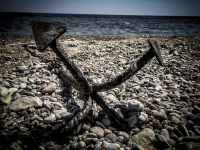 a big black anchor lays at the stone beach of souloudrania on rhodes