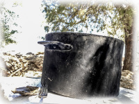 a big black metal soup pot and a fork are standing in the shadow at the beach souloudrania on rhodes