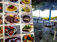 next to a big colorful menu card you see chairs and tables of a taverna in kritinia on rhodes