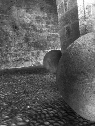 two big cannonballs are standing on a stone floor between old walls in the old town of rhodes, black-and-white