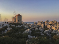 three windmills and rocks at the harbor of rhodes city at sunsetlight