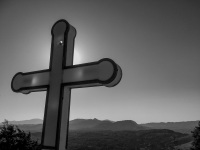 a big cross of the tsambika church on rhodes in front of the sun and in front of hills in the distance, black-and-white