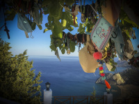 colourful talismans are hanging in a fig tree at the tsambika church of rhodes, in the background you see the blue sea