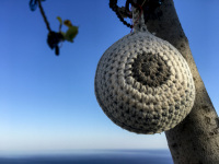 a grey chrocheted ball is as a talisman hanging in a fig tree befor the blue sky at the tsambika church on rhodes