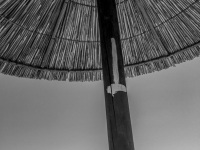 a straw parasol at the lardos beach on rhodes, in the distance you see a military ship, black-and-white