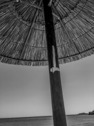 a straw parasol at the lardos beach on rhodes, in the distance you see a military ship, black-and-white