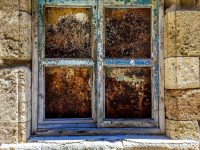 a blue wheathered window is embedded in yellow old walls in the old town of rhodes