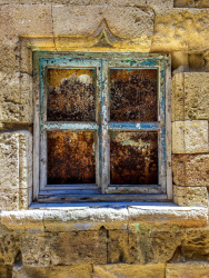a blue wheathered window is embedded in yellow old walls in the old town of rhodes