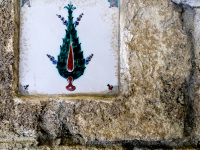 a white tile with a green cypress hangs on a beige wall in filerimos on rhodes