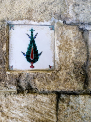 a white tile with a green cypress hangs on a beige wall in filerimos on rhodes