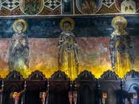 dark brown church chairs in front of illuminated fresco painting in the church of asklipio on rhodes