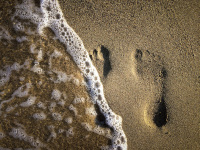 a little wave rolls over two footprints in beach sand on rhodes