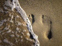 a little wave rolls over two footprints in beach sand on rhodes