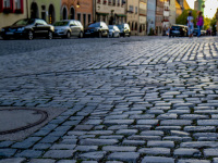 a street with cobblestones, cars and colorful houses in the background in rothenburg ob der tauber in germany