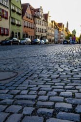 a street with cobblestones, cars and colorful houses in the background in rothenburg ob der tauber in germany