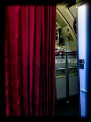 next to a red curtain you see the kitchen of the cabin crew in a plane of aegean airlines in hamburg in germany