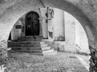 view through a wall arch to an old door with steps before in the village bovino in italy, black-and-white