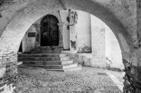 view through a wall arch to an old door with steps before in the village bovino in italy, black-and-white