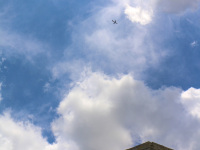 a plane in the distance is flying over the castel del monte in puglia with a sunny sky and some clowds