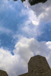 a plane in the distance is flying over the castel del monte in puglia with a sunny sky and some clowds