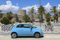 a light blue fiat 500 in front of the castle of manfredonia in italy